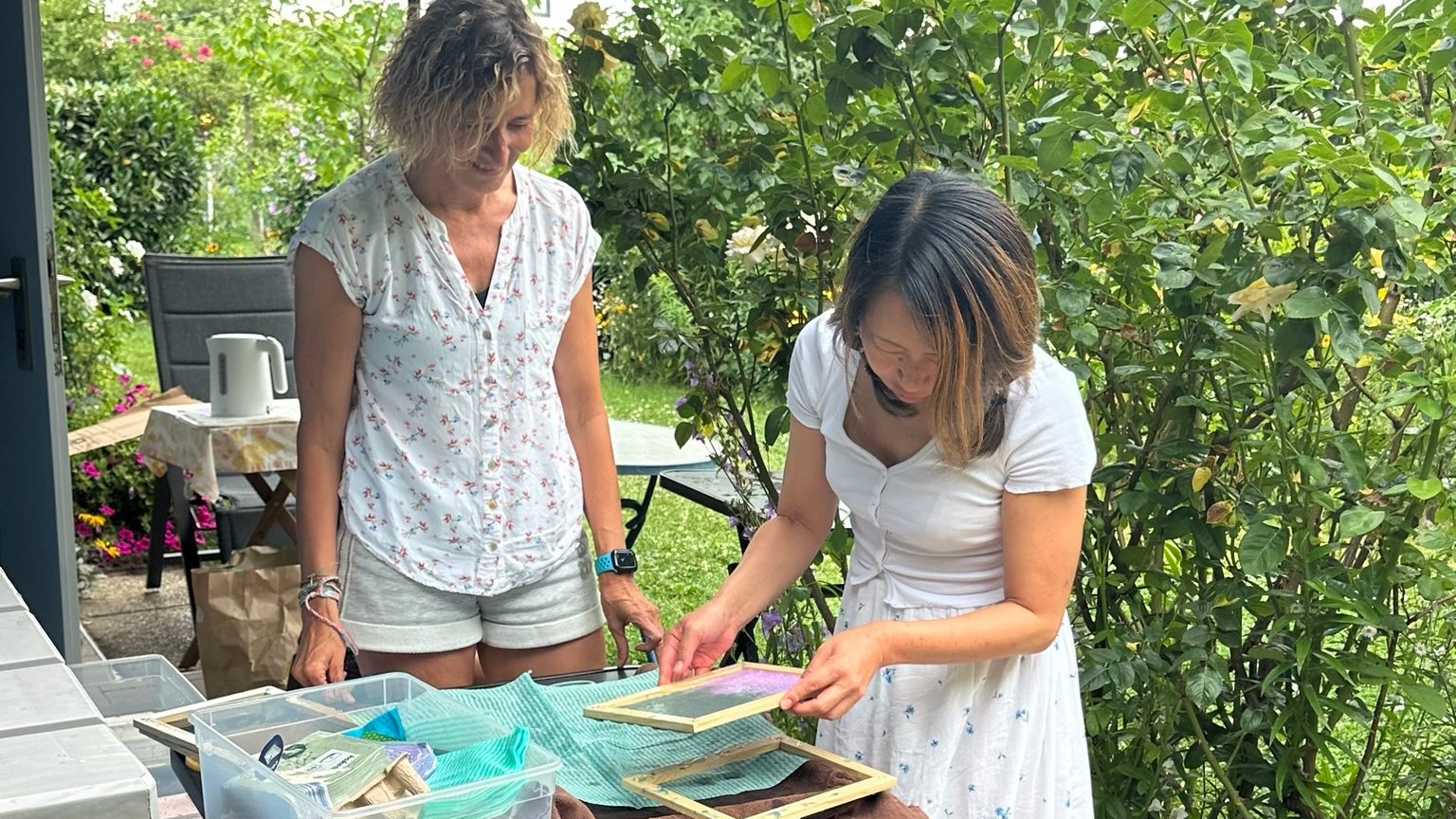 Moni begleitet eine Teilnehmerin beim gemeinsamen Papierschöpfen im Garten.